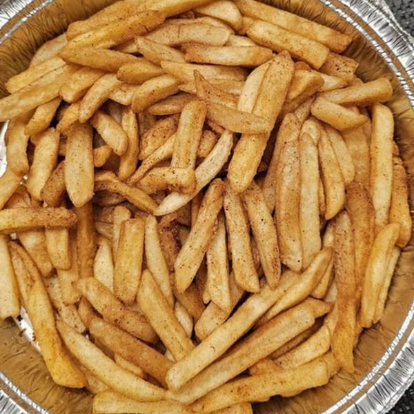 A close-up of seasoned french fries in a round, silver foil container from Apna Pizza.