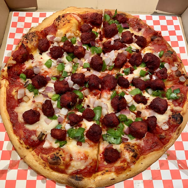 Apna Pizza's chicken tikka pizza with red sauce, cheese, green peppers, and onions in a box.